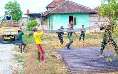 Personel Satgas TMMD bersama masyarakat bahu-membahu menurunkan material besi yang akan digunakan untuk pembangunan jalan cor beton di Dusun Kedungpandan, Rabu (22/7/2026).
