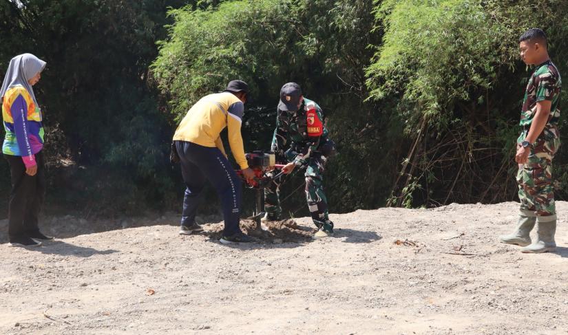 Babinsa Desa Kesongo Serka Lasmidi bersama petugas DLH Kabupaten Bojonegoro menyiapkan lubang tanam pohon di kawasan tanggul sungai Desa Kesongo dalam rangkaian TMMD ke-129.
