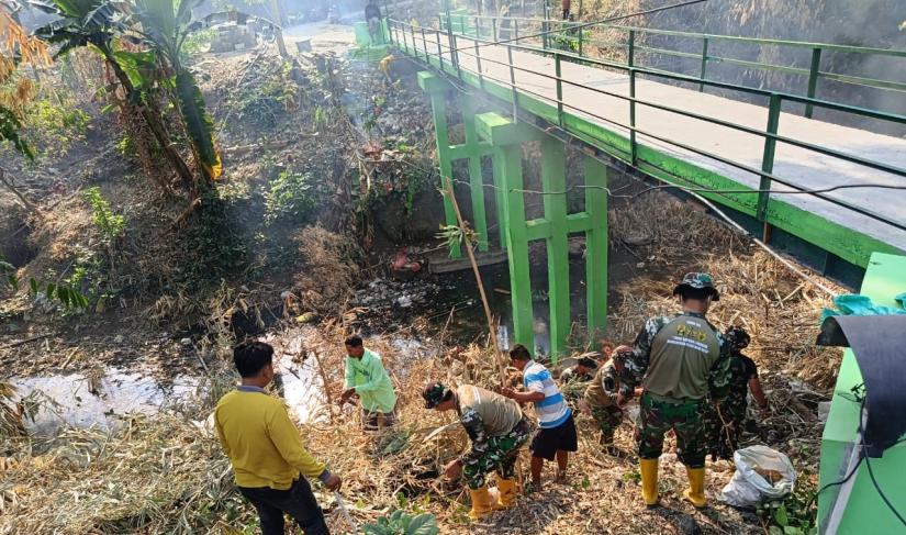  Personel Satgas TMMD ke-129 Kodim 0813/Bojonegoro bersama warga melaksanakan kerja bakti membersihkan area Jembatan Brang Etan, Desa Kesongo, Kecamatan Kedungadem, Kabupaten Bojonegoro.