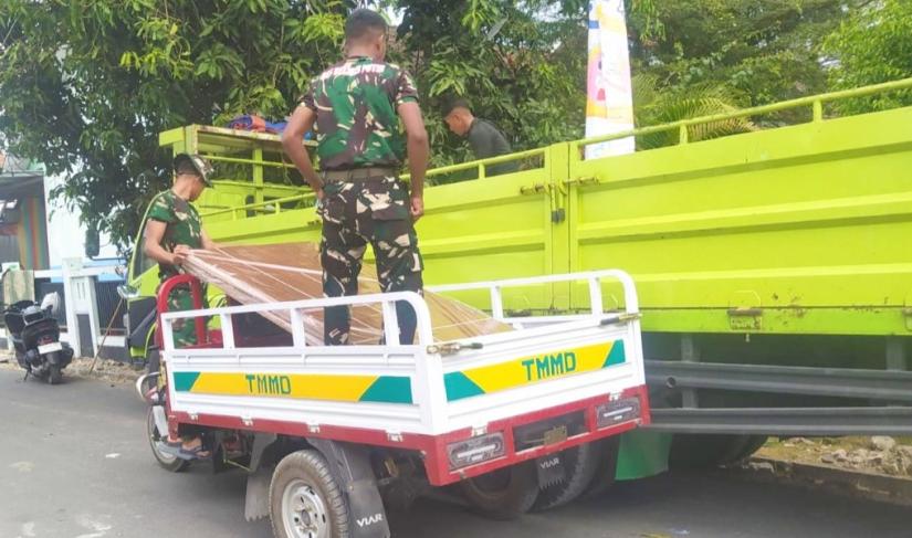 Di Desa Kesongo, Kecamatan Kedungadem, Kabupaten Bojonegoro, Sabtu (1/8/2026), personel Satgas TMMD memanfaatkan kendaraan roda tiga untuk mengangkut material bangunan menuju rumah-rumah penerima manfaat yang berada di gang sempit.